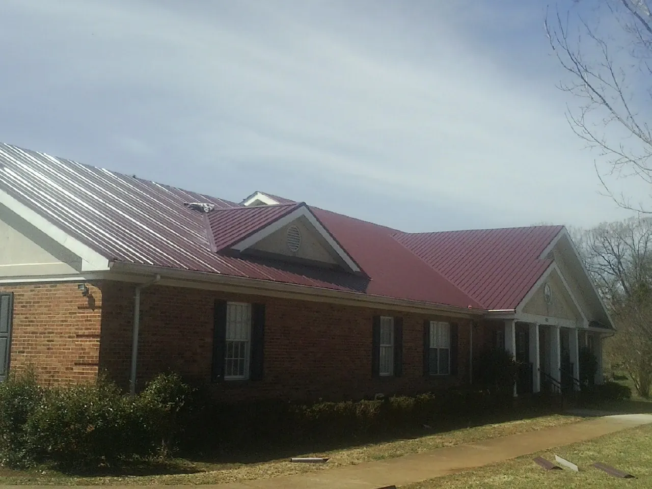 Red metal roof with gabled entries on a long brick building, from a Hail Damage Roof Repair job in Polk