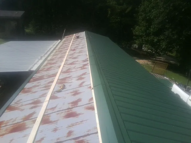 Old rusted panels beside newly installed green metal roofing — Wind Damage Roof Repair by Roofing Brothers in Polk