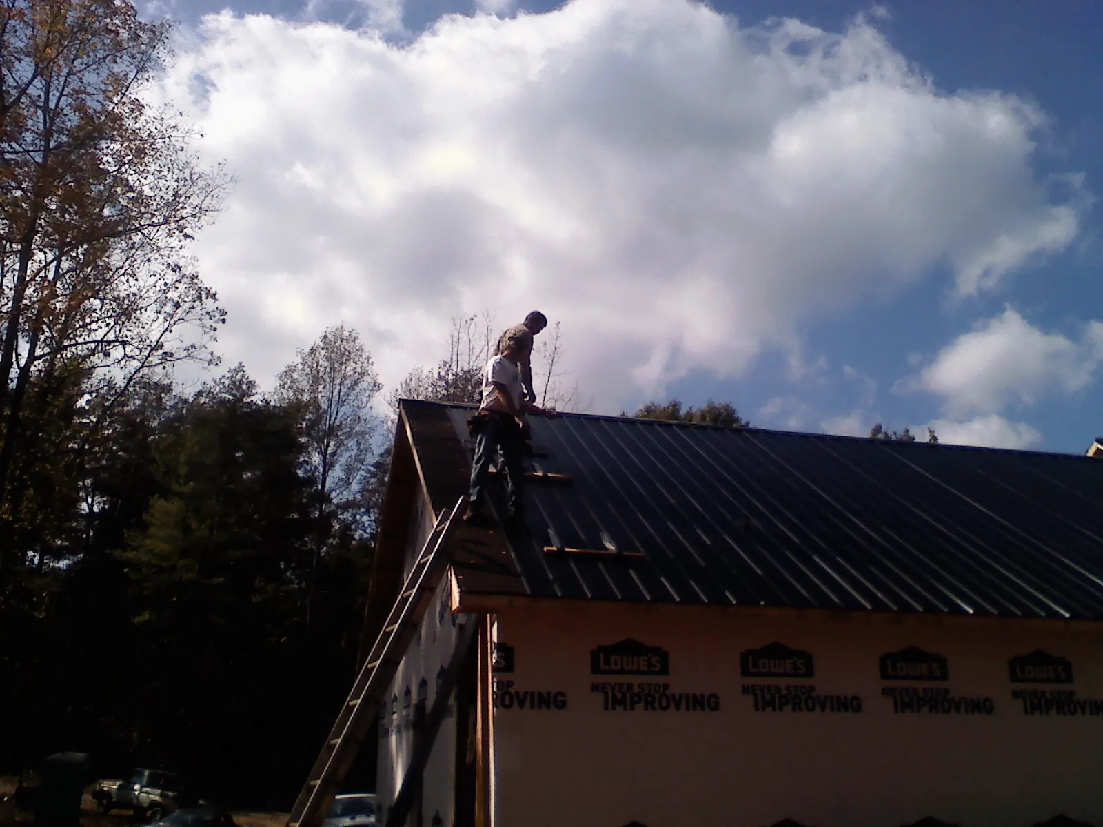 Roofer fastening dark metal panels high against a cloudy sky, from a Roof Inspection job in Polk