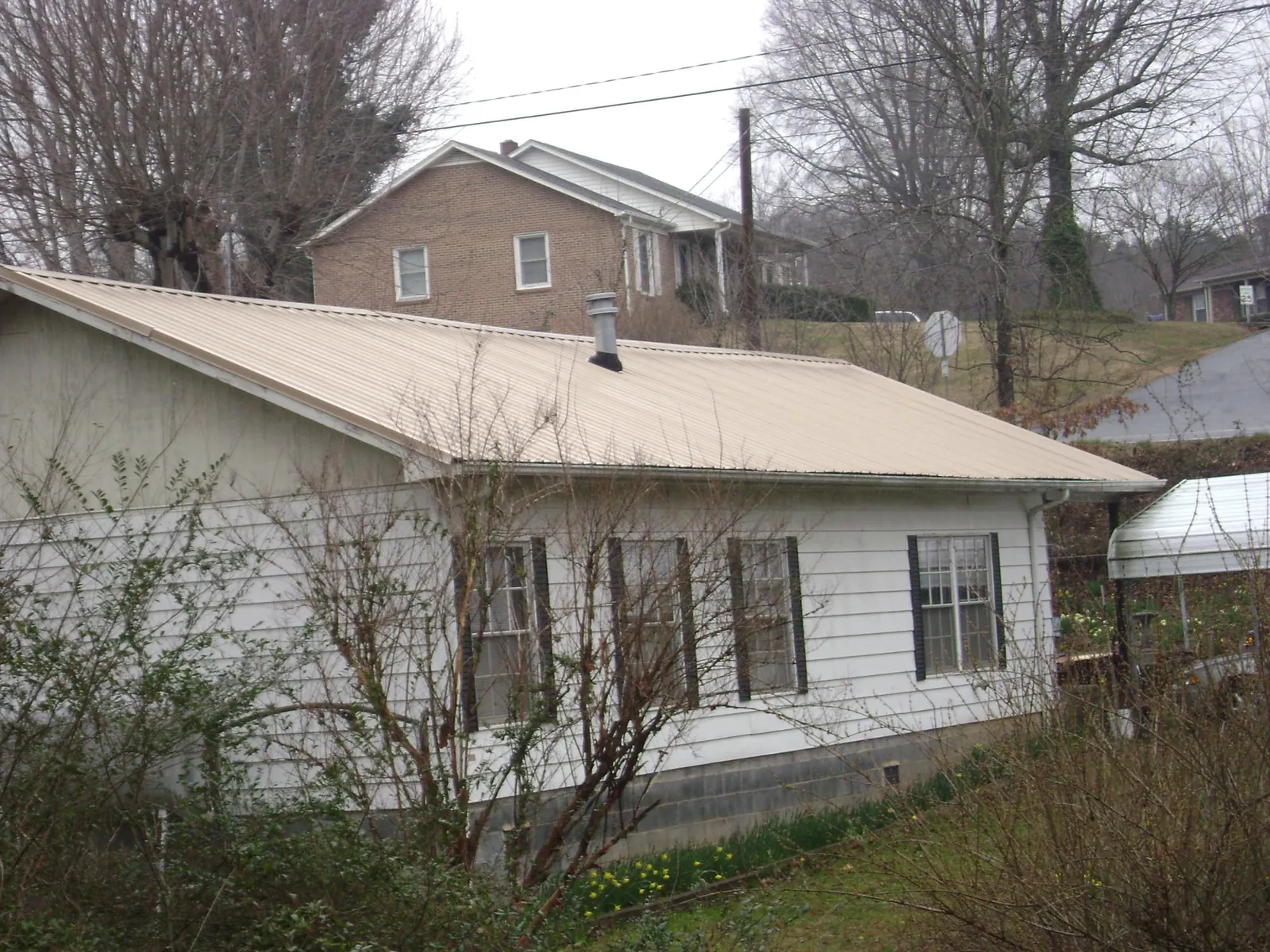 Tan metal roof on a white sided house set into a hillside — Commercial Roofing by Roofing Brothers in Polk
